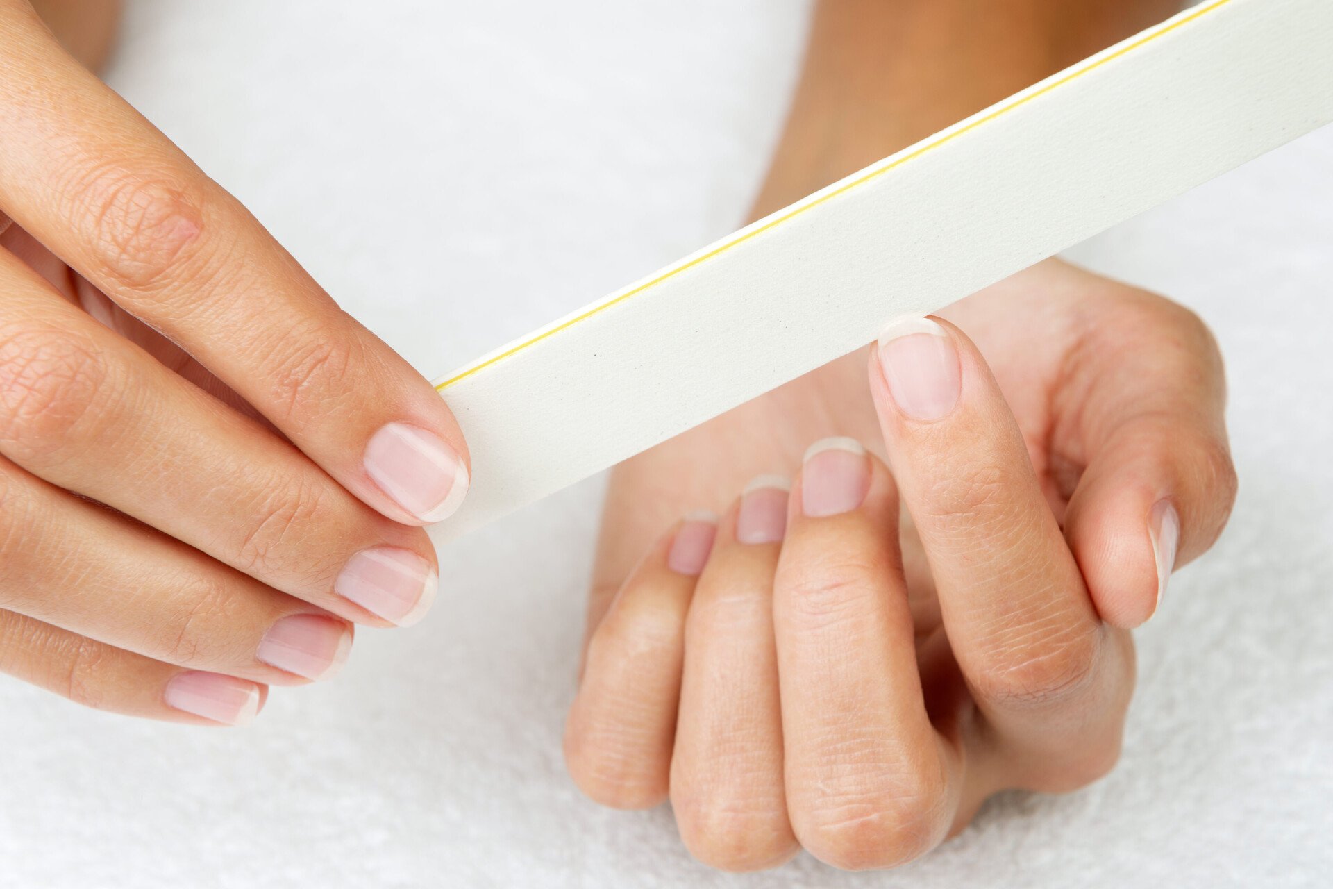 Nahaufnahme von zwei schönen, gepflegten Händen bei der Nagelpflege; genauer gesagt beim Nägel feilen.