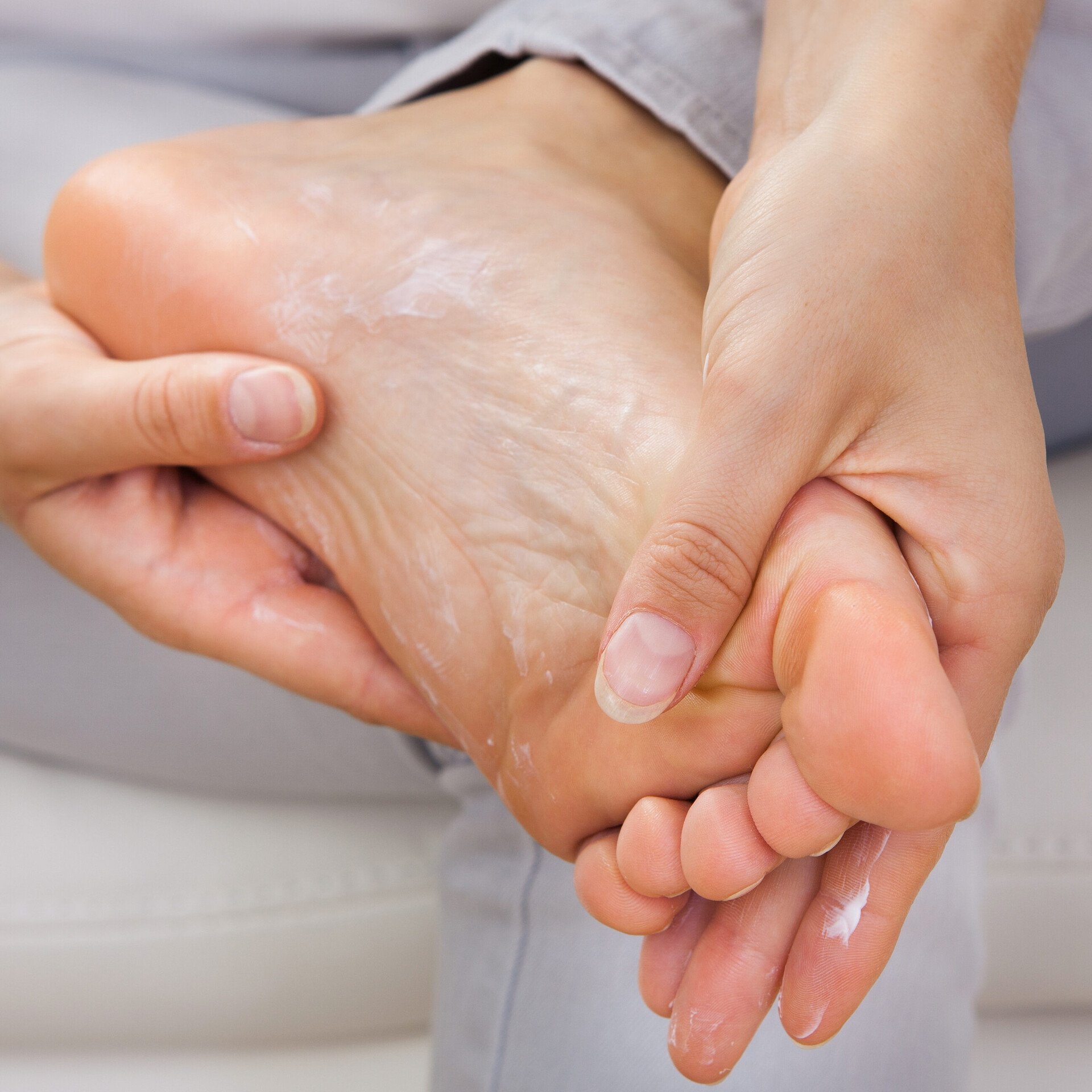 Zwei Hände cremen bei der Fußpflege eine Fußsohle ein, um Hornhaut zu reduzieren.