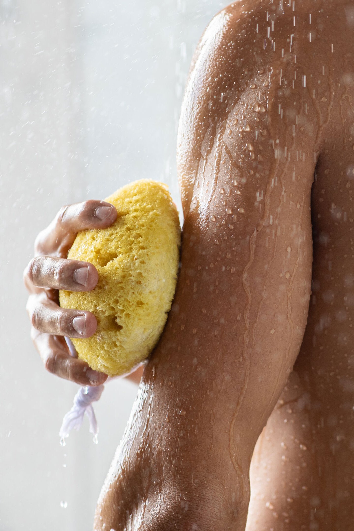 Ein Mann seift sich beim Duschen den Oberarm mit einem Schwamm ein. Das Bild illustriert einen Bereich der täglichen Hautpflege.