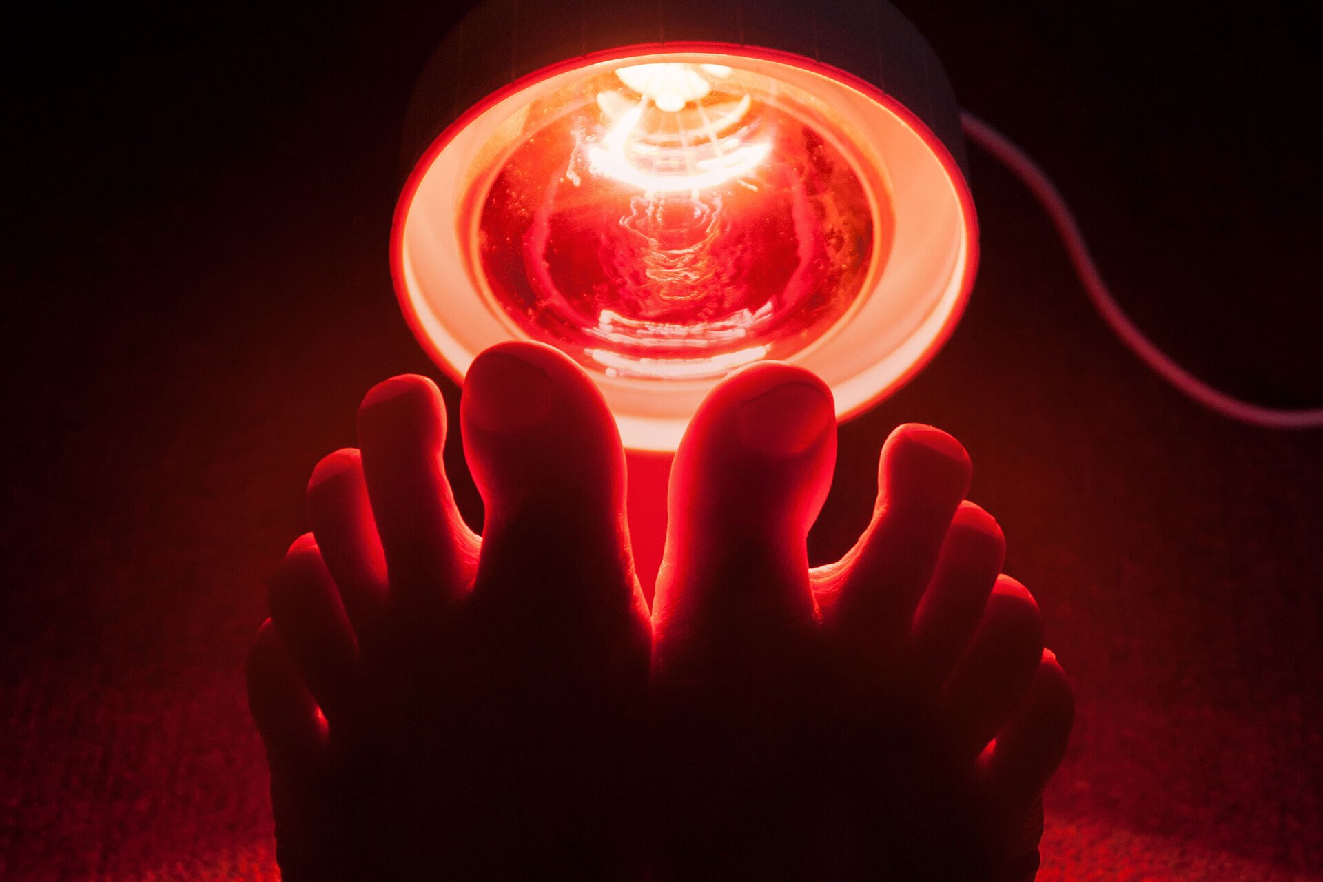 Eine effektive Wärmebehandlung gelingt mit einer speziellen Wärmelampe. Das Bild zeigt zwei Füße vor dem roten Licht.
