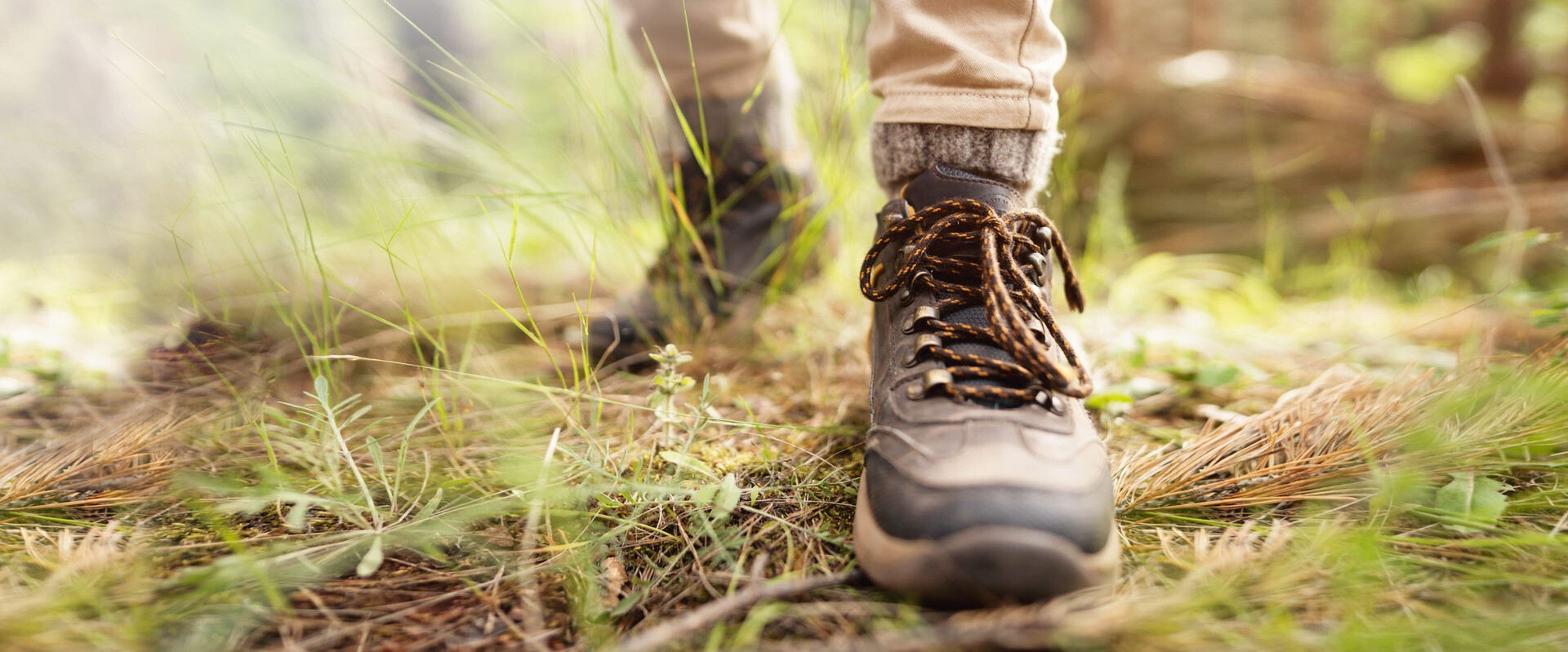 Zwei Füße in Wanderstiefeln auf Waldboden stehen hier für die Thematik trockene Füße.