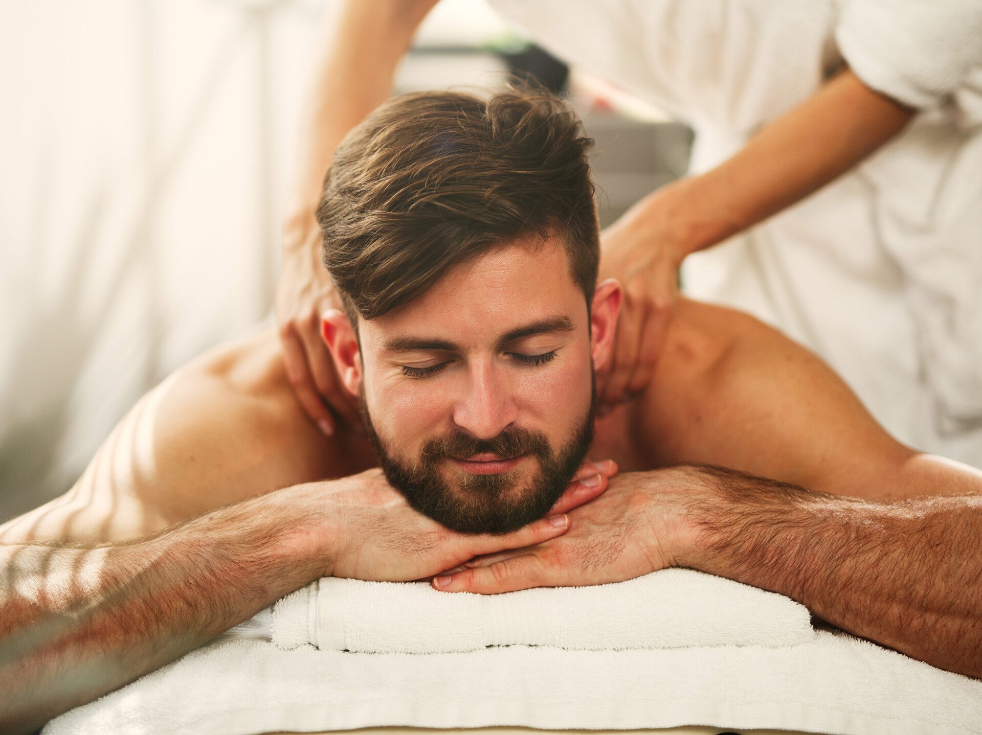 Eine Massage der Schultern, wie bei diesem liegenden Mann, kann auch die Psyche entspannen.