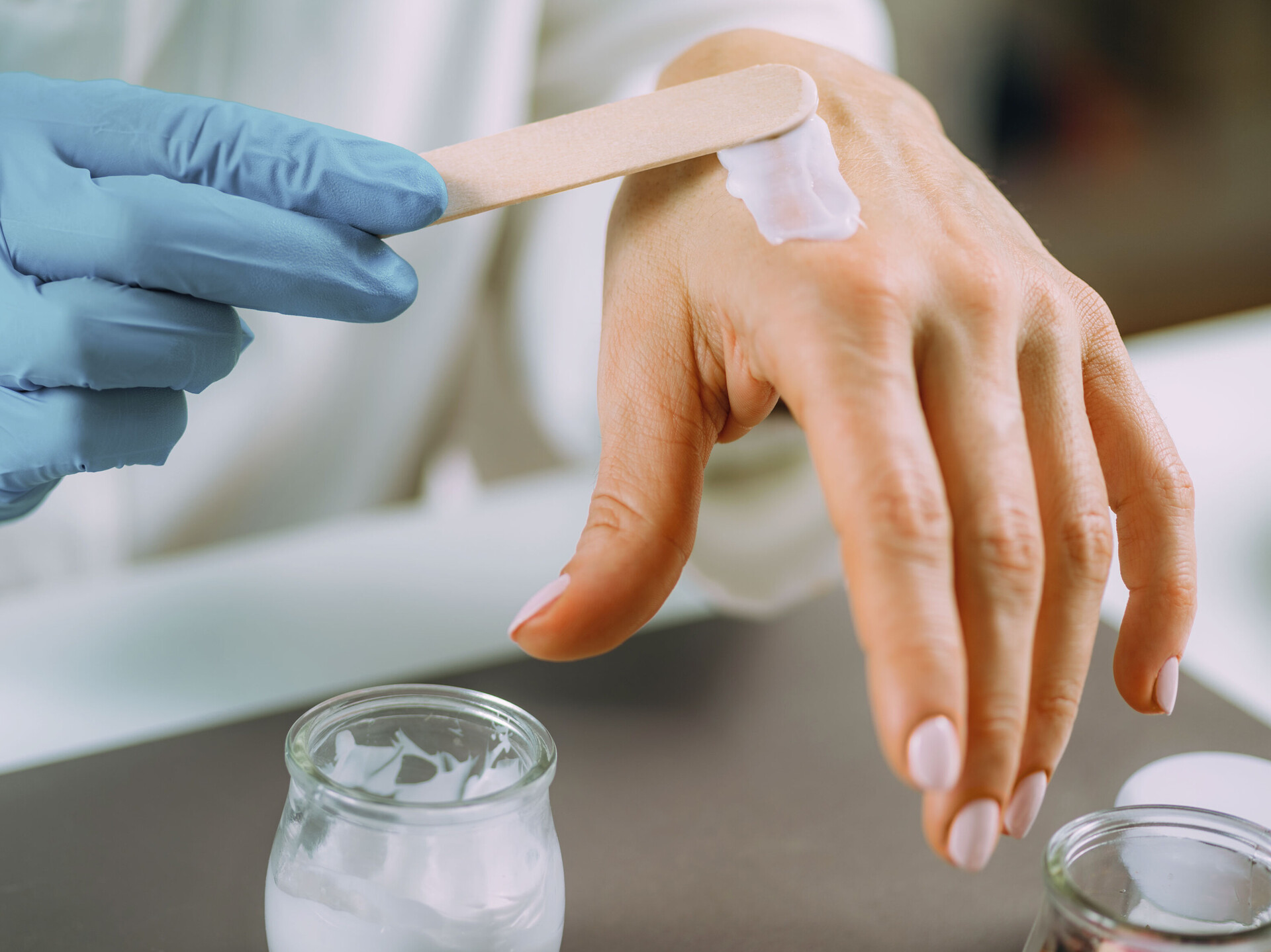 Eine behandschuhte rechte Hand streicht Creme mit einem Spatel auf die linke Hand. Die Sixtus-Forschung spielt eine wichtige Rolle bei der Entwicklung von Hautpflege-Produkten.