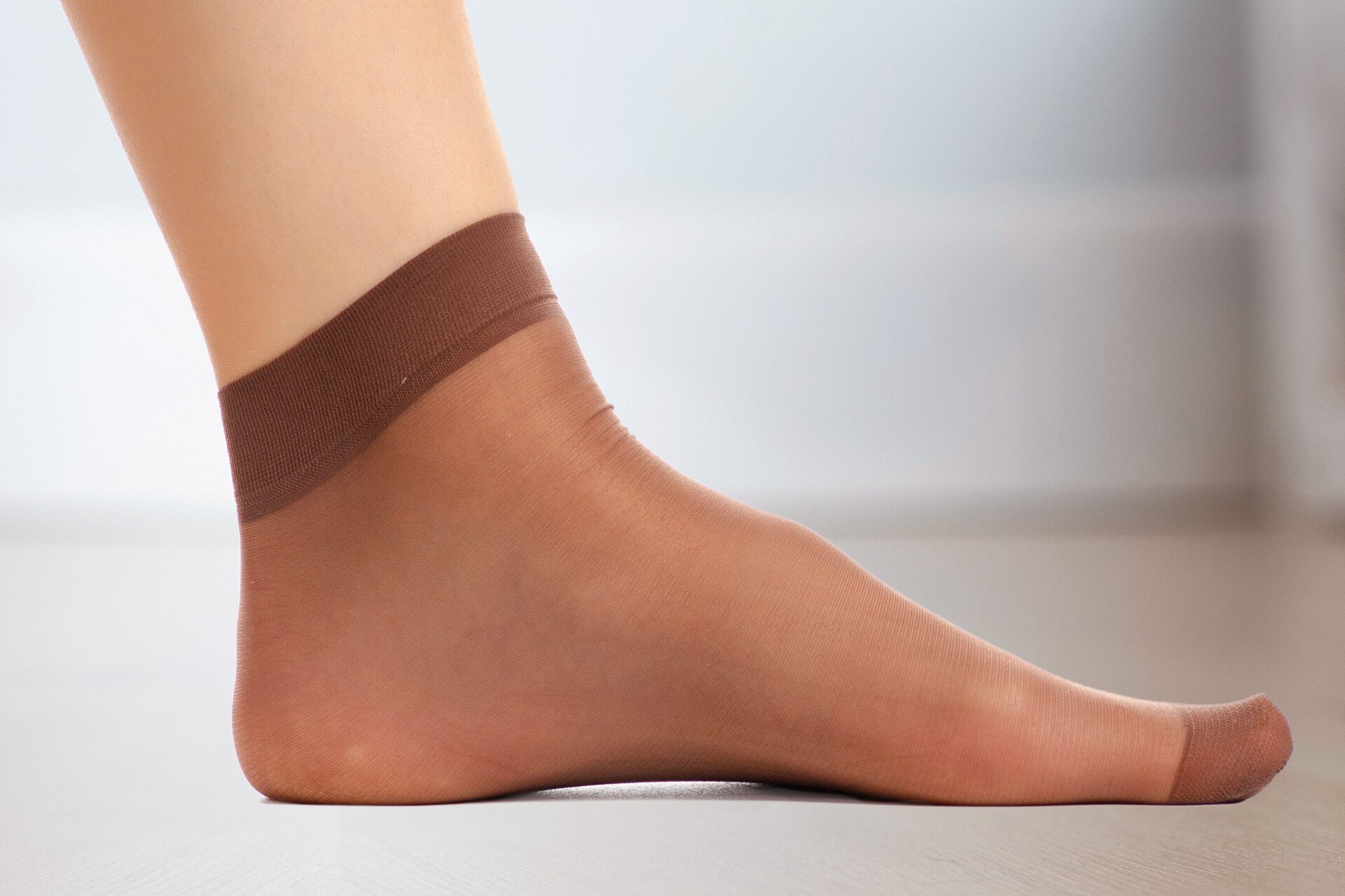 Nahaufnahme eines Fußes mit einer dünnen Nylonsocke. Das Bild steht für Pflegetipps, um Blasen an den Füßen vorzubeugen.