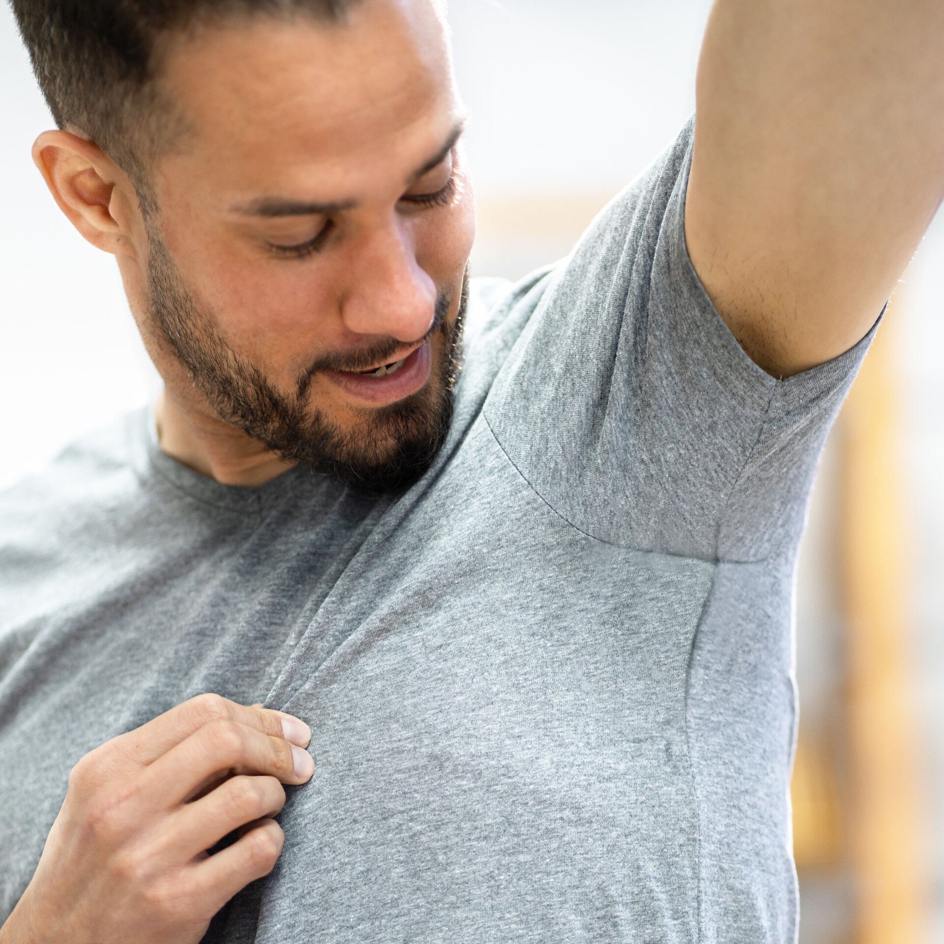 Ein Mann im T-Shirt blickt prüfend in seine Achsel. Das Bild illustriert die Wirkweise desodorierend.